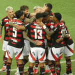 Torcedores do Flamengo cantando e vibrando em estádio lotado, em um dia de jogo.