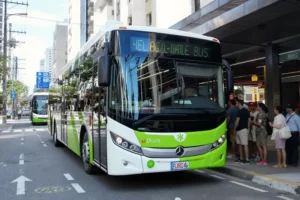 Ônibus urbano branco e verde com logo Euro 6 em ponto de ônibus movimentado, pessoas sorrindo.