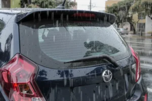 Traseira de carro hatch escuro em dia chuvoso, com vidro traseiro sujo sem limpador.
