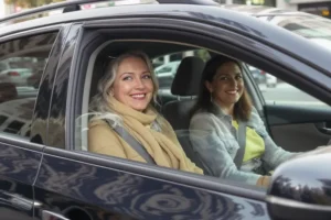 Passageira sorridente entrando em um Uber, motorista mulher sorri pelo retrovisor.