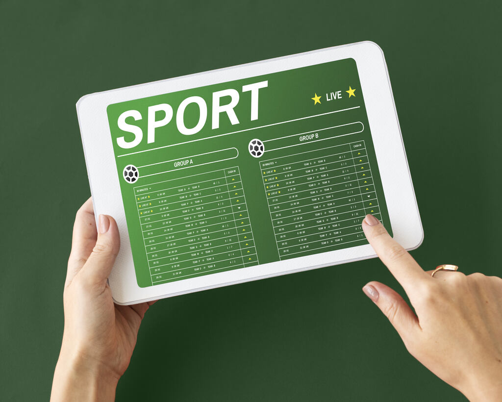Tablet com aplicativo de apostas esportivos na tela e uma mão clicando