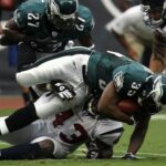 Jogador do Philadelphia Eagles sendo derrubado enquanto segura a bola de futebol americano