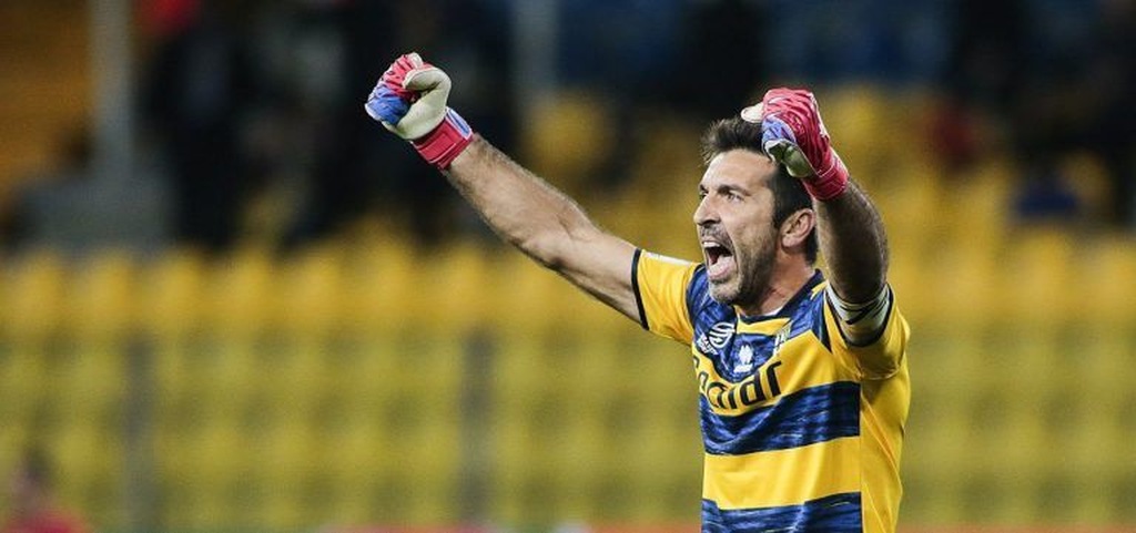 Goleiro italiano Buffon, com uniforme azul e amarelo, listrado, comemorando vitória em partida com os braços para o alto.