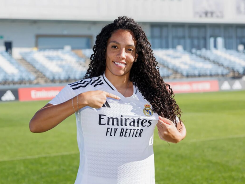 Yasmim Queiroz vestindo o uniforme do Real Madrid feminino em um estádio de futebol.