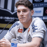 Jogador Rollheiser correndo em campo com a camisa do Santos sob luzes vibrantes do estádio.