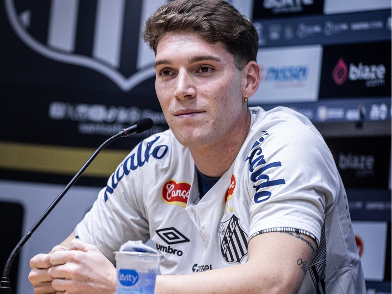Jogador Rollheiser correndo em campo com a camisa do Santos sob luzes vibrantes do estádio.
