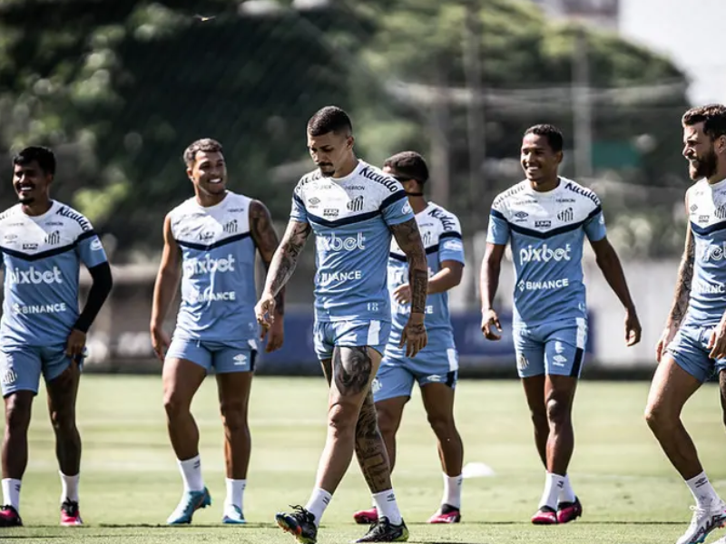 Jogadores do Santos em treino intenso, suando e correndo em campo, com técnico supervisionando.