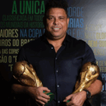 Ronaldo Fenômeno sorrindo em estúdio durante entrevista sobre futebol.