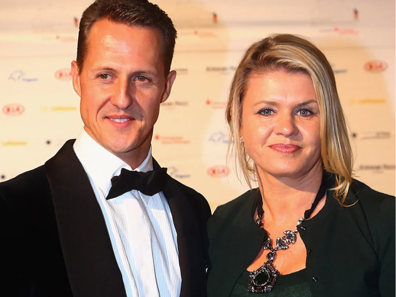 Corinna Schumacher no tribunal, rosto iluminado pela luz, cercada por advogados.