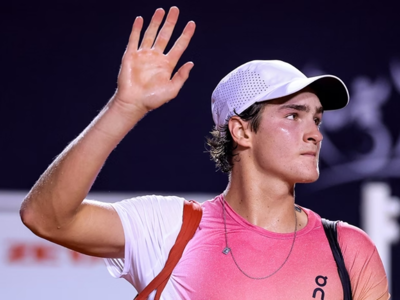 João Fonseca se preparando para sacar em uma quadra de tênis durante um treinamento, com alta concentração.