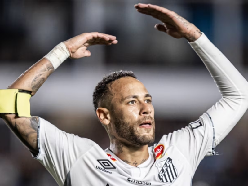 Jogador de futebol driblando em campo com grama sintética.
