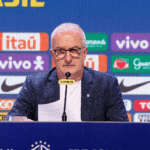 Endrick, Ederson e Paquetá em um campo de futebol com a torcida brasileira ao fundo.