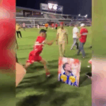 Jogador do CRB chutando foto de rival do CSA em vestiário de futebol.