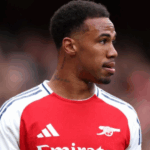 Gabriel Magalhães vestindo uniforme do Arsenal sob holofotes vibrantes.