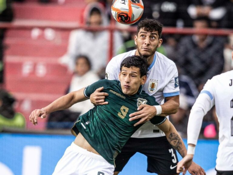 Jogadores de Bolívia e Uruguai disputando a bola no alto durante partida em La Paz.