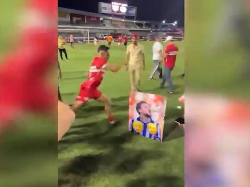 Jogador do CRB comemora o título chutando foto de rival do CSA em vestiário vibrante.