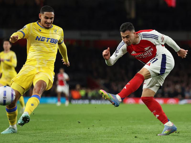 Jogadores do Arsenal e Crystal Palace disputando a bola durante partida noturna da Premier League.