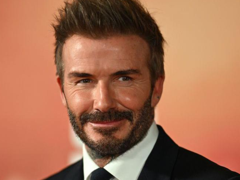 David Beckham celebrando seu 50º aniversário com um terno elegante e champanhe em um terraço de luxo.
