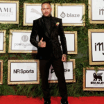 Neymar em terno elegante durante leilão beneficente, rodeado por convidados e iluminação suave.