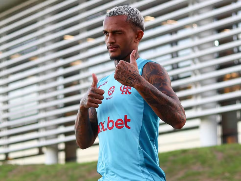 Fotografia ultrarrealista de Wesley, jogador do Flamengo, chutando a bola em campo. Ele veste uniforme vermelho e preto e a cena é iluminada por holofotes com torcedores borrados ao fundo.