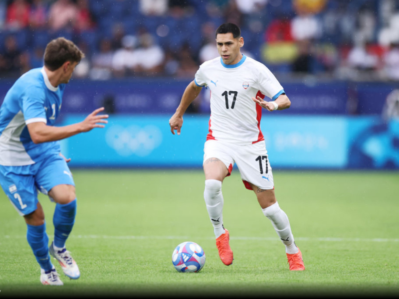 Gustavo Caballero, jogador de futebol, posando no campo de um estádio, vestindo a camisa branca do Santos.