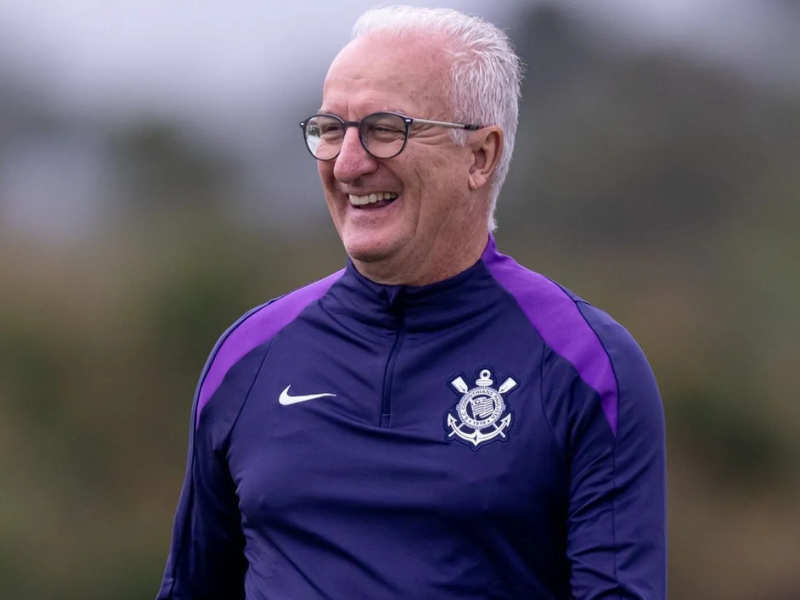Close-up ultrarrealista de Dorival Júnior atrás de uma mesa com microfones, vestindo agasalho do Corinthians. Fundo desfocado da Neo Química Arena.