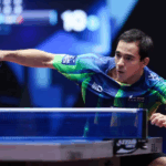 Hugo Calderano, atleta brasileiro de tênis de mesa, sorrindo e exibindo sua medalha de ouro no pescoço em uma arena de tênis de mesa. Imagem vibrante e ultrarrealista com iluminação focada.
