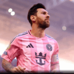 Lionel Messi, em close-up, correndo com a bola em um campo de futebol, sob luzes intensas em um estádio.