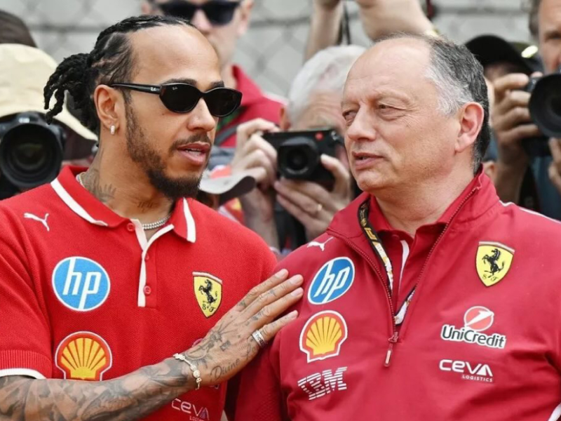 Fred Vasseur, chefe da Ferrari, e Lewis Hamilton, piloto, em uma discussão focada na garagem da Ferrari de Fórmula 1, com o carro SF-25 ao fundo.