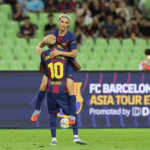 Dois jogadores do Barcelona, com uniformes vibrantes, comemoram um gol em um campo de futebol, expressando emoção e alegria.