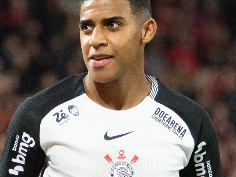 Gui Negão, jovem jogador do Corinthians, de 18 anos, comemorando um gol com os braços erguidos em um campo de futebol.