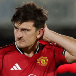 Multidão de torcedores do Grimsby Town em preto e branco invadindo o gramado verde de um estádio de futebol à noite, celebrando.