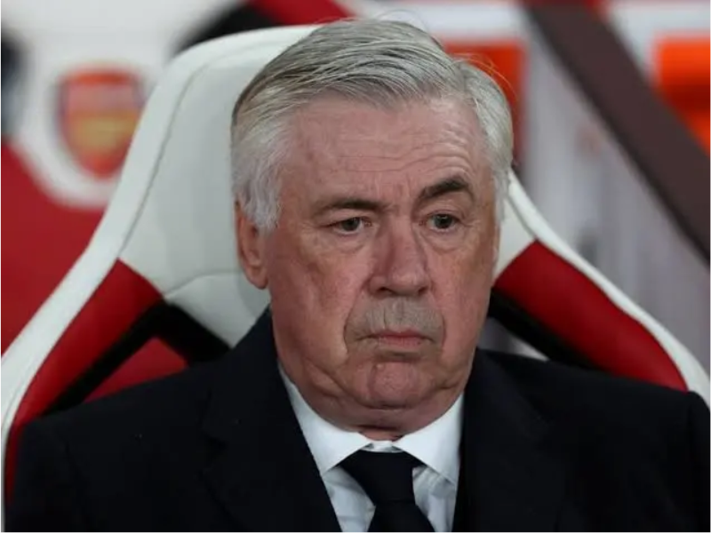 Retrato ultrarrealista de Carlo Ancelotti, técnico de futebol, em um campo de gramado sintético, vestindo terno azul, com o sol do fim da tarde e um estádio ao fundo. Sua expressão é de foco e sabedoria.