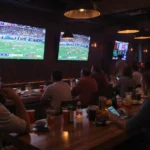 Pessoas em um bar assistindo futebol americano e apostando em seus celulares.