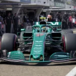 Aston Martin AMR26 em teste na pista, com detalhes visíveis e engenheiros ao fundo.